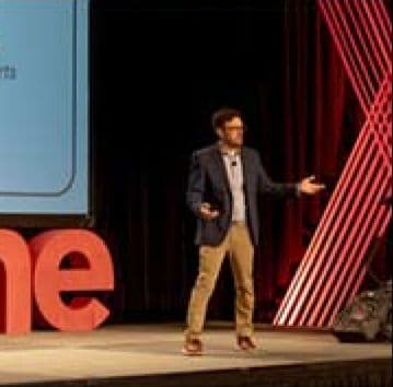 Speaker presenting on stage beside giant red Marcone letters