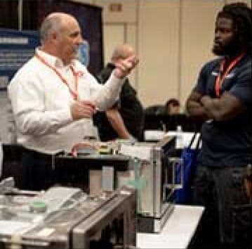Two attendees talking over appliance components at a Vendor Fair booth